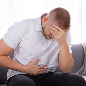 Sad Young Man Sitting On Sofa Suffering From Stomach Pain