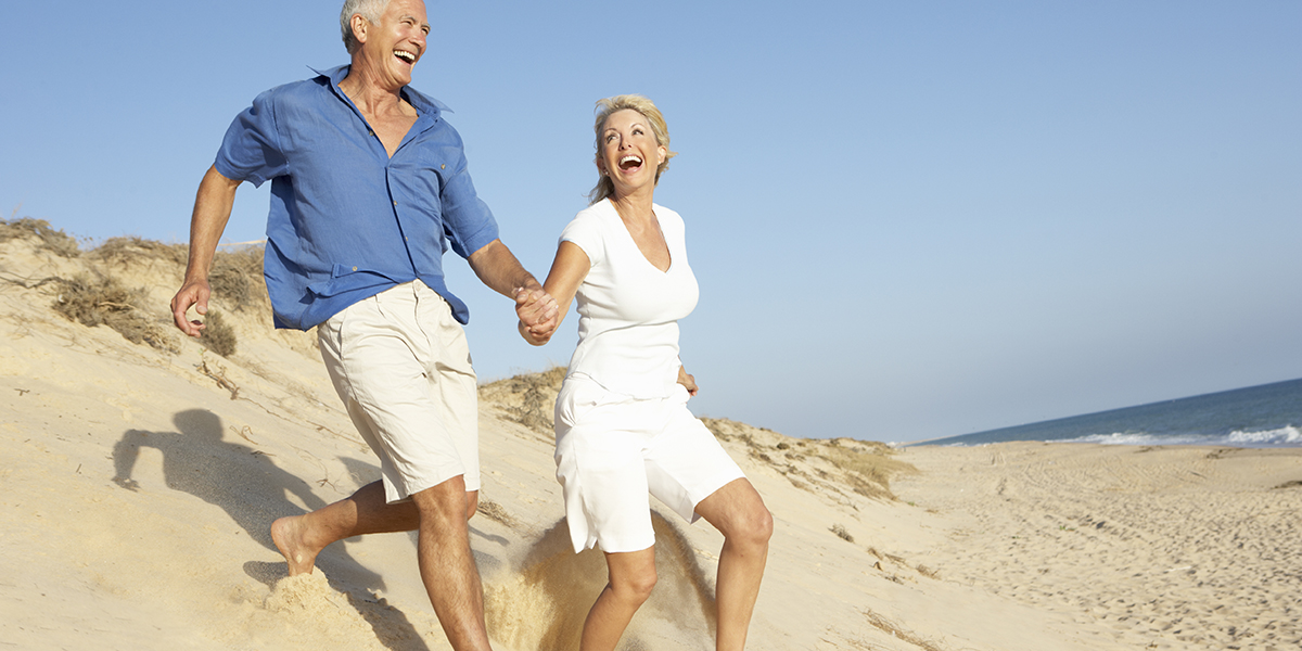 Senior Couple Enjoying Beach Holiday Running Down Dune