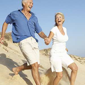 Senior Couple Enjoying Beach Holiday Running Down Dune