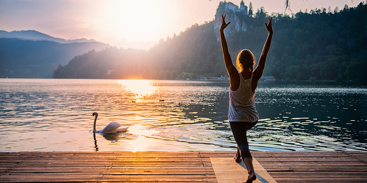 Beautiful woman practicing Yoga by the lake - Sun salutation series - Swan passing by - Toned image