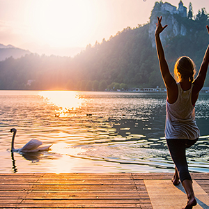 Beautiful woman practicing Yoga by the lake - Sun salutation series - Swan passing by - Toned image